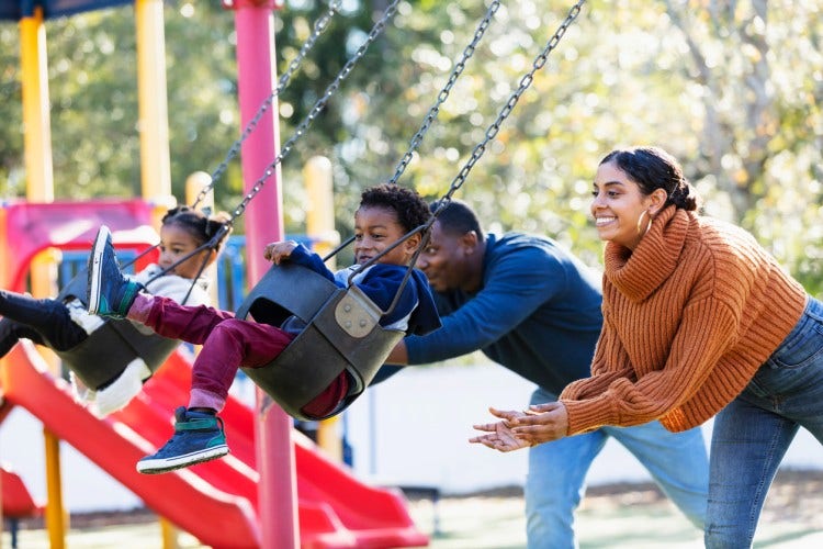 Smiling adults pushing children on swings.