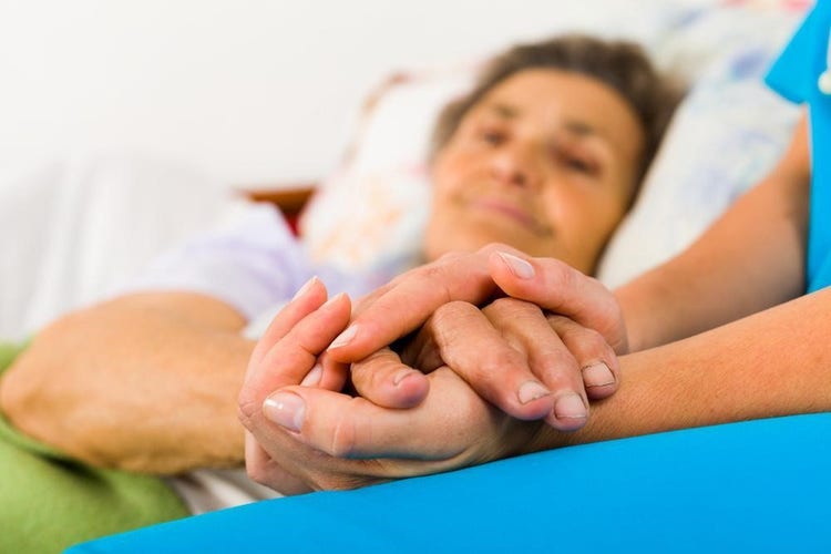 A hospitalized, bedridden patient holds the hands of her social worker.