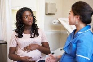 A pregnant woman speaks with a nurse in an exam room.